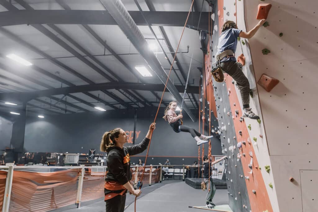 Several climbers ascend an indoor climbing wall, demonstrating skill and collaboration in a vibrant environment.