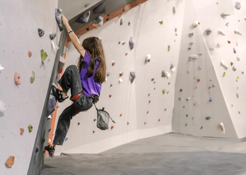 A young girl engaged in indoor rock climbing, navigating her way up a colorful rock wall with focus and enthusiasm.